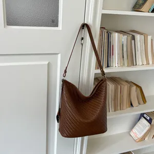 Bruine gevlochten emmertas hangend bij een boekenkast in een vintage lifestyle-stijl.