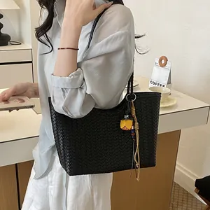 Elegante bolso de hombro trenzado negro bajo el brazo con un amuleto de flor amarilla
