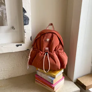 Primer plano de una mochila acolchada naranja con logo de oso sobre una pila de libros