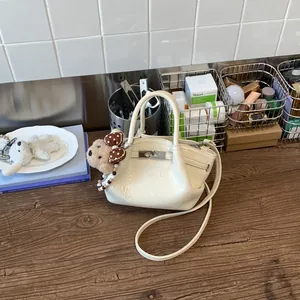 Dettaglio di una borsa a secchiello in pelle stropicciata crema con un grazioso ciondolo a orsetto