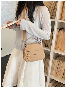 Elegante bolso bandolera de nailon beige para mujer usado por una modelo en una biblioteca.