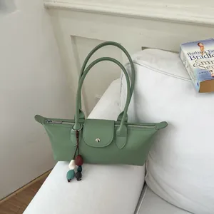 Sac à bandoulière dumpling en cuir vert avec longues anses sur canapé