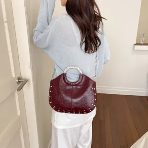 Back view of model carrying the dark red studded handbag with a chain strap.