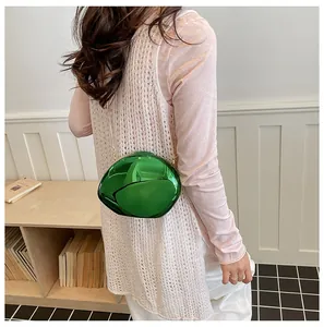 Dettaglio di una borsa da sera verde a specchio a forma di conchiglia indossata da una modella