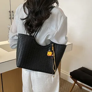 Detalle de un bolso tote de cuero trenzado negro con adorno floral al hombro de mujer