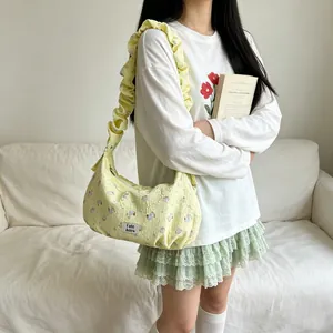 Detailed view of a trendy yellow floral dumpling shoulder bag with ruffled strap worn by a model