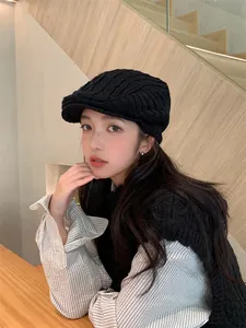 Detail of a black knitted newsboy cap worn by a model in a cozy winter setting