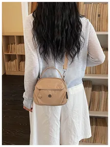 Bolso bandolera de lona beige mostrado en la espalda de una modelo en una biblioteca