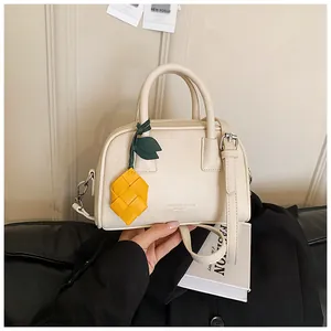 Close-up of cream pillow handbag with decorative yellow pineapple charm accessory