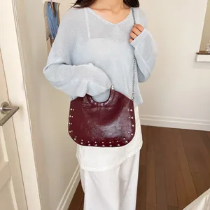 Chic burgundy rivet handbag held by a model to show size and glossy leather texture.