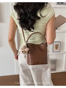 Detailed view of brown woven bucket bag with cute bear charm carried by model