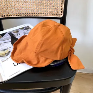 Primer plano de un sombrero de sol naranja de ala ancha con un lazo decorativo en una silla.