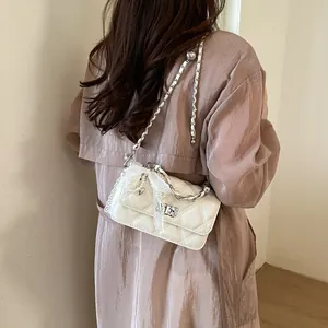 Detailed view of a white quilted crossbody bag with lace and pearl charms on model