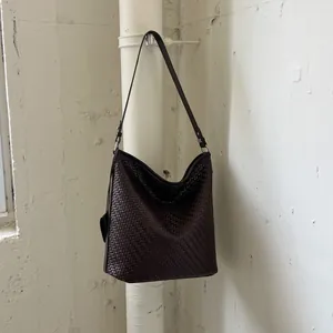 Detail van een grote vintage geweven leren emmer tas hangend aan een witte buis