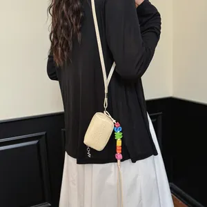 Detail of a minimalist beige mini crossbody bag with a colorful letter bead charm.
