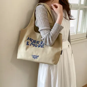 Primer plano del bolso tote de lona caqui con bordado azul llevado al hombro