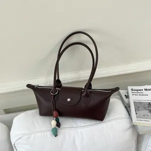 Vue rapprochée d'un sac à main marron minimaliste en forme de dumpling avec de longues anses.