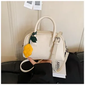 Detailed view of the textured cream-white pillow bag and its yellow pineapple charm.