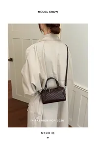 Borsa a cuscino retrò intrecciata marrone indossata a tracolla da una modella in cappotto.