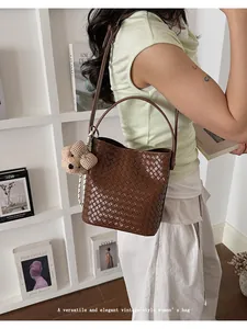 Detailed view of a vintage-style brown woven bucket bag featuring a cute teddy bear charm
