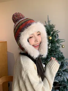 Close-up of a colorful knitted winter earflap hat with cozy beige faux fur and pom-pom.