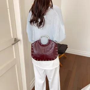 Back view of a model wearing a burgundy patent leather handbag with silver studs and chain.