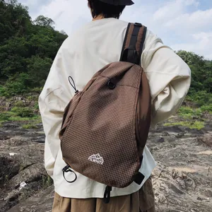 Dettaglio di una borsa a tracolla da trekking a scacchi marroni indossata all'aperto.