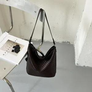 Detail van een bruine geweven hobo tas die aan een minimalistische stoel hangt.