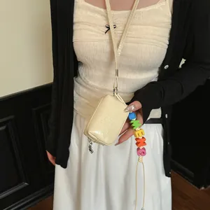 Close-up of cream mini cross-body bag with colorful letter bead charm