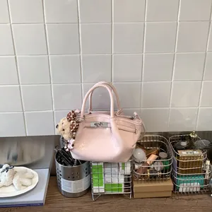 Dettaglio di una borsa a secchiello rosa lucido con ciondolo a forma di orsetto su un tavolo