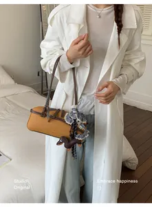 Elegant mustard yellow Boston bag with dachshund charm and ribbon detail on model