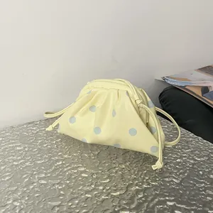 Detail view of a pale yellow polka dot pouch bag with thin strap on textured surface.