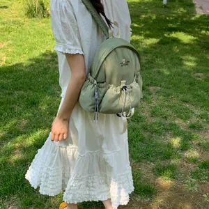 Mochila informal de nailon verde salvia con un vestido blanco de volantes al sol