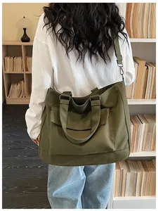Large olive green canvas tote bag shown as a crossbody bag carried in a cozy library