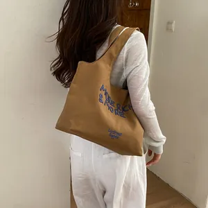 Vista detallada de un bolso tote de lona marrón con bordado azul
