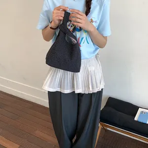 Detailaufnahme einer schwarzen Gitter-Knoten-Eimertasche, gehalten von einem Model im Sommeroutfit