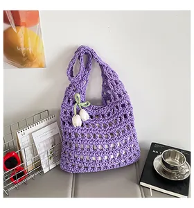 Detalle de un bolso de hombro calado de punto morado con una decoración de dije de tulipán