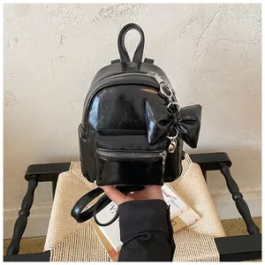Stilvoller kleiner schwarzer glänzender Rucksack mit großer Schleife auf einem Stuhl.