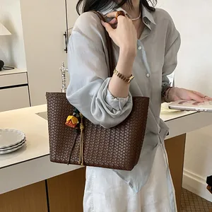 Bolso tote grande de tejido marrón con colgante floral, llevado al hombro por una modelo.