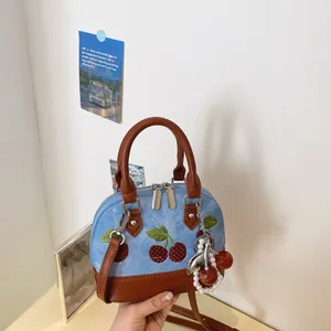 Vista detallada de un bolso bandolera de mezclilla con bordado de cerezas y colgante de perlas