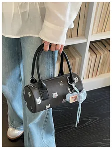 Detail of a stylish barrel handbag with cartoon cat prints and a blue heart charm.