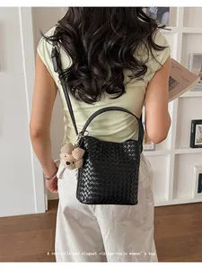 Back view of a stylish black woven bucket bag featuring a cute teddy bear charm accessory