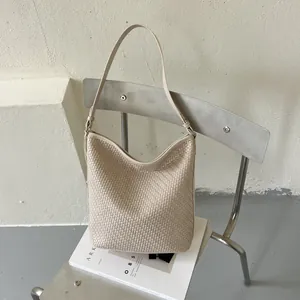 Gedetailleerd vooraanzicht van een beige gevlochten hobo-emmer tas op een minimalistische stoel