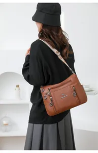 Detailed back view of a brown faux leather shoulder bag with a wide patterned strap on model
