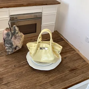 Dettaglio di un'elegante borsa a secchiello gialla lucida su tavolo rustico.