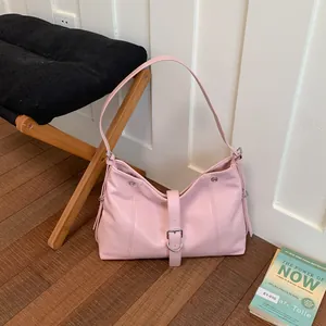 Detailed view of a pink underarm bag with buckle strap on a wooden floor setting.