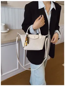 Vue détaillée d'un élégant sac à main beige avec breloque en perles tenu par un modèle