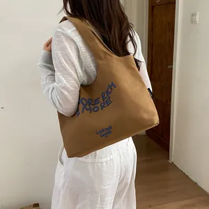 Vista detallada del bolso tote de lona marrón con texto bordado azul al hombro.