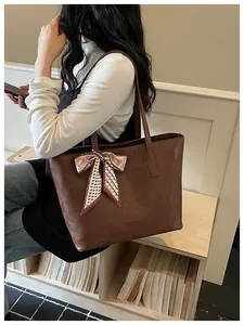 Close-up detail of a brown embossed leather tote bag with a decorative ribbon scarf