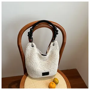 Close-up of a white woven bucket bag with a black beaded handle on a wooden chair